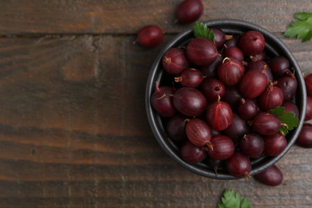 Ripe red gooseberries in bowl on wooden table, flat lay. Space for textの写真素材