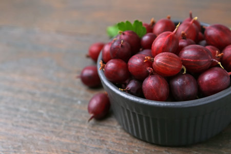 Ripe red gooseberries in bowl on wooden table, closeup. Space for textの写真素材