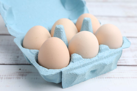 Raw eggs in egg carton on white wooden table, closeup
