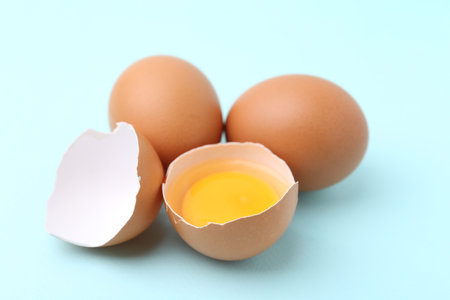 Whole and broken chicken eggs on light blue background, closeup