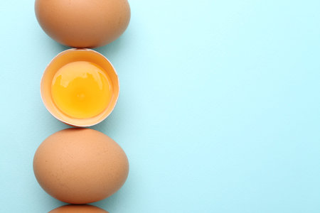 Whole and broken chicken eggs on light blue background, top view. Space for text