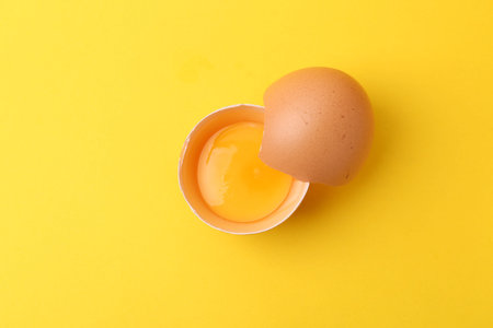 One broken chicken egg on yellow background, top view