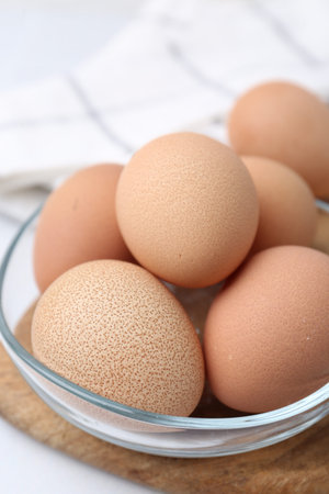 Raw chicken eggs in bowl on white table, closeup