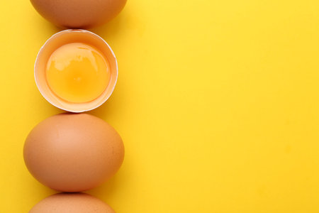 Whole and broken chicken eggs on yellow background, top view. Space for text