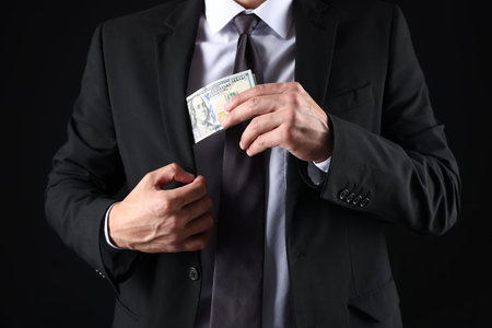 Man putting dollars in pocket on black background, closeup