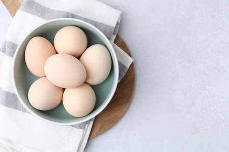 Raw eggs in bowl on white table, top view. Space for text