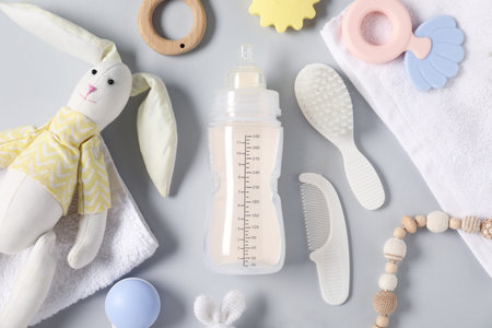 Bottle with milk and baby accessories on light grey background, flat lay
