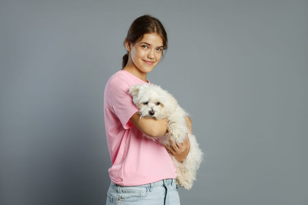 Happy teenage girl with Maltese dog on grey background
