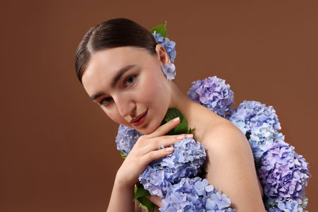 Beautiful young woman with hortensia flowers on brown background