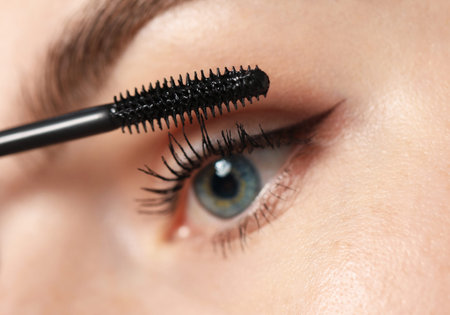 Young woman applying mascara onto her eyelashes, closeup