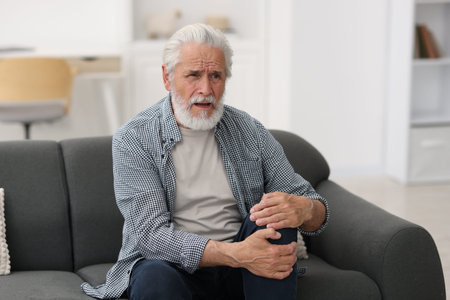 Senior man suffering from knee pain at home