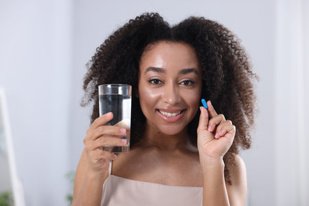 Beautiful Brazilian woman with glass of water and collagen pill indoors