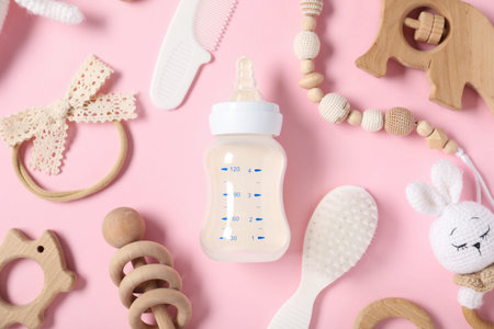 Bottle with milk and baby accessories on light pink background, flat lay