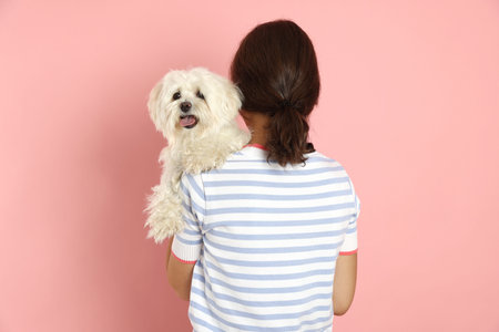 Happy teenage girl with dog on pink background, back view