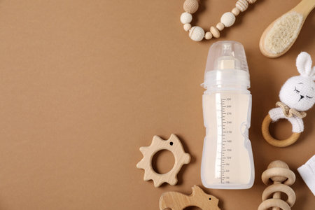 Bottle with milk and baby accessories on brown background, flat lay. Space for text