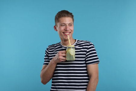 Smiling man drinking lemonade from mason jar on light blue background. Refreshing drink