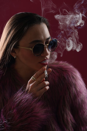 Woman in fur coat smoking cigarette on pink background, closeup