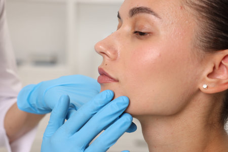 Doctor examining young woman's mole in hospital, closeup