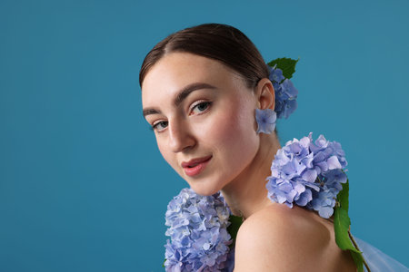 Beautiful young woman with hortensia flowers on blue background