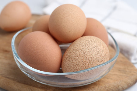 Raw chicken eggs in bowl on white table, closeup