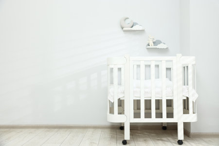 Comfortable crib near white wall in baby's room, space for text. Interior designの写真素材