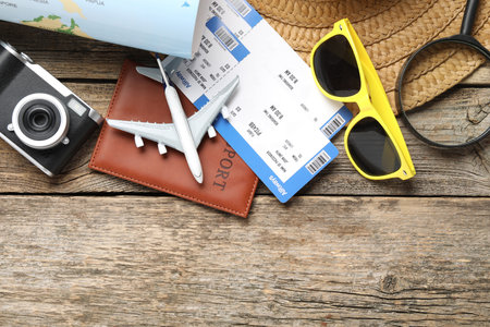 Time for summer vacation. World map, passport, flight tickets, toy plane, camera, magnifying glass and beach accessories on wooden table, flat lay. Space for textの写真素材