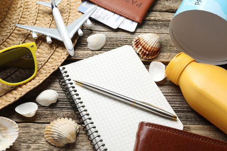 Time for summer vacation. Stationery, passport, flight tickets, toy plane, world map and beach accessories on wooden table, closeupの写真素材