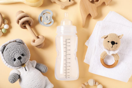 Bottle with milk and baby accessories on beige background, flat lay