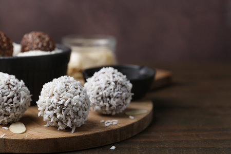 Delicious homemade candies with coconut flakes on wooden table, closeup. Space for text