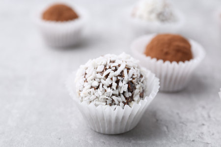 Delicious homemade candies with cocoa powder and coconut flakes on light gray table, closeup