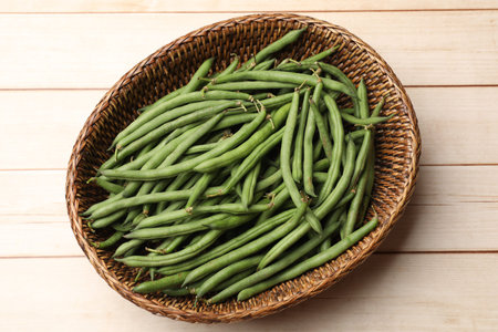 Fresh pea pods in wicker basket on light wooden table, top view