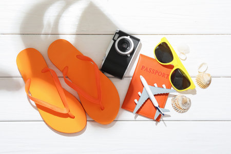 Time for summer vacation. Toy plane, passport, camera and beach accessories on white wooden table,...