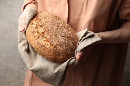 Woman with loaf of fresh bread against grey background, closeup
