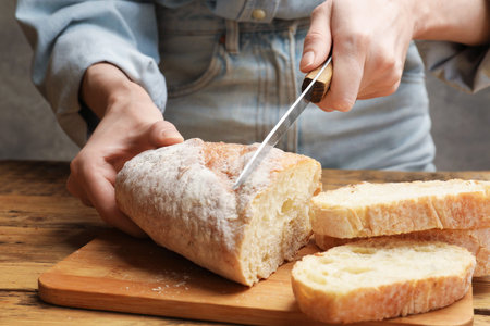 Woman cutting fresh bread at wooden table, closeup