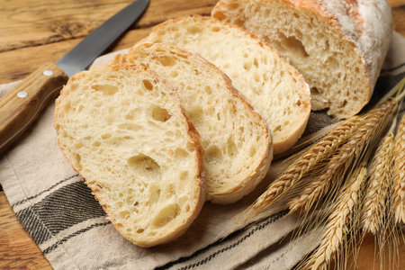 Fresh bread, wheat spikes and knife on wooden table, closeup