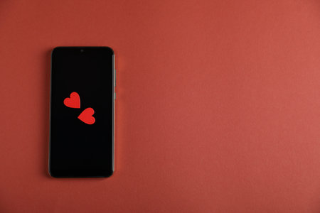 Online dating site. Smartphone and hearts on red-brown background, top view. Space for textの写真素材