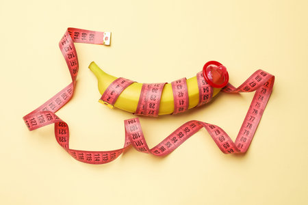 Sex education. Banana with condom and measuring tape on beige background, top viewの写真素材