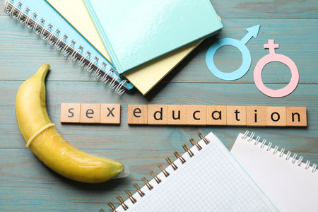 Phrase Sex Education made of wooden letters, banana, paper female and male gender symbols, notebooks on blue table, flat layの写真素材