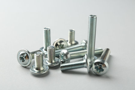 Many different metal bolts on light grey background, closeup. Hardware tool