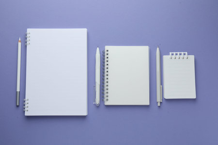 White notepads and pens on violet background, flat lay. Space for textの写真素材