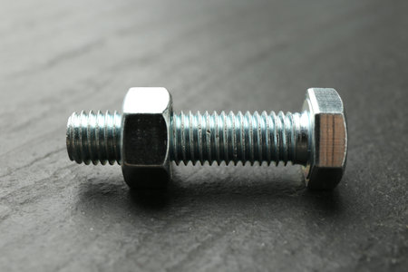 Metal bolt and nut on black table, closeup