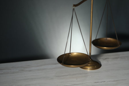 Scales of justice on light wooden table against gray background, closeup. Space for text