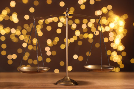 Golden scales of justice on wooden table against blurred lights
