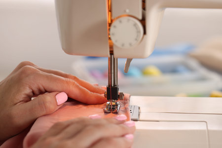Woman working with sewing machine and fabric in workshop, closeup
