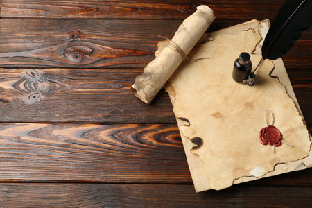 Old paper scrolls, feather and inkwell on wooden table, flat lay. Space for text