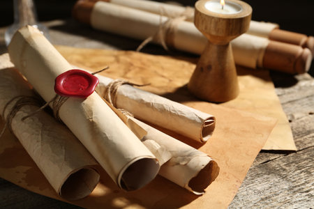 Old paper scrolls and burning candle on wooden table, closeup