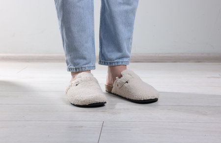 Woman in soft white slippers on light wooden floor, closeup