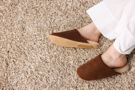 Woman in brown slippers on soft beige carpet, top view. Space for text