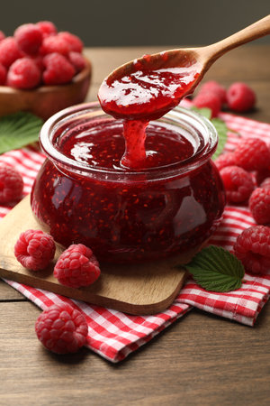 Taking tasty jam with spoon on wooden table, closeup