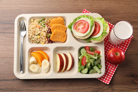 Plastic tray with tasty food, milk and fork on wooden table, top view. School lunchの写真素材